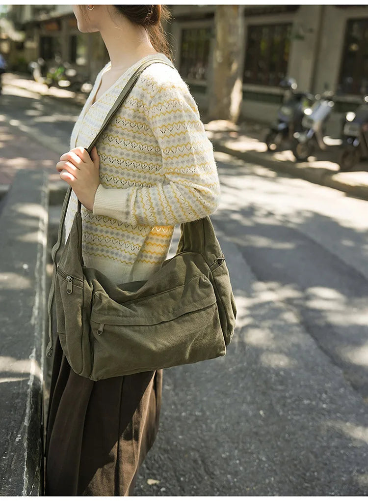 A woman wearing a cream and yellow patterned sweater carries a large olive green cotton canvas shoulder crossbody bag on a ci