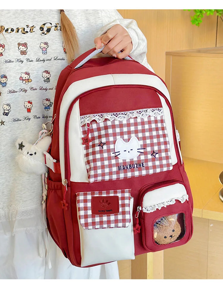 A maroon and white backpack featuring a checkered pattern and a cat design, worn by a person.