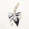 A white and black floral patterned fabric bow attached to a gold chain for an adjustable bag strap.