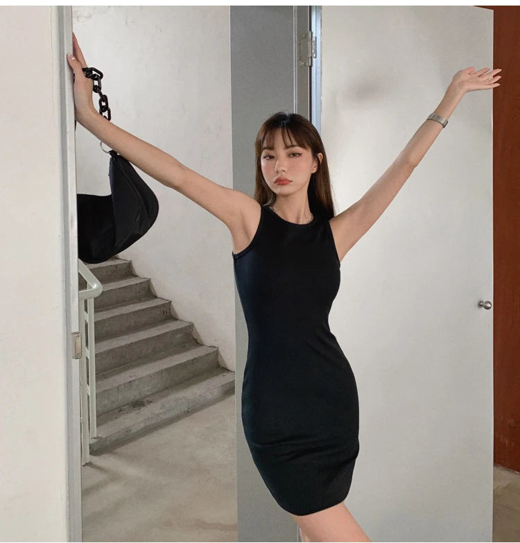 A woman wearing a black sleeveless bodycon tank dress posing in a hallway.