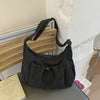 A dark plaid nylon drawstring tote bag resting on a wooden shelf next to a white wall.