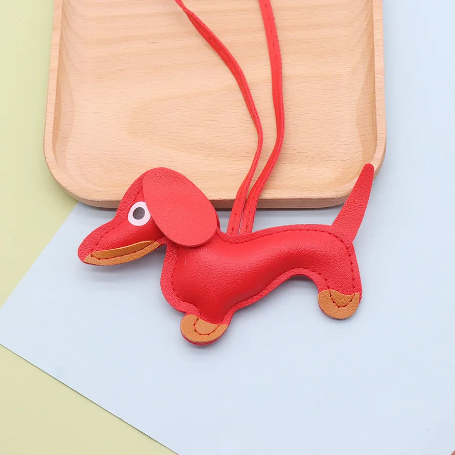 A red leather dachshund dog charm keychain resting on a light wooden cutting board and a white paper.