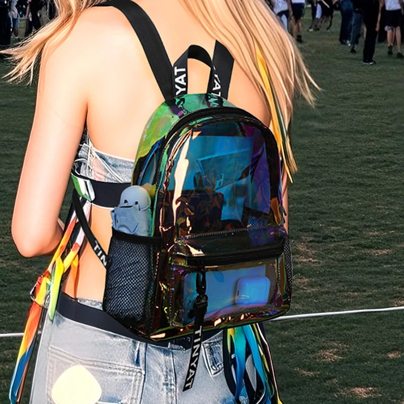 A woman wearing a clear PVC backpack with colorful straps and a dark green transparent fabric on a grassy field.