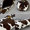 A brown and white cow print cylinder shoulder bag with a gold zipper detail.