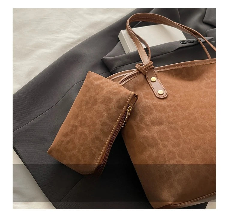 A brown leopard print tote bag with tan leather handles is shown resting on a dark gray blazer.