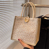 A beige floral linen tote bag with woven handles and a wooden closure is displayed against a window blind.