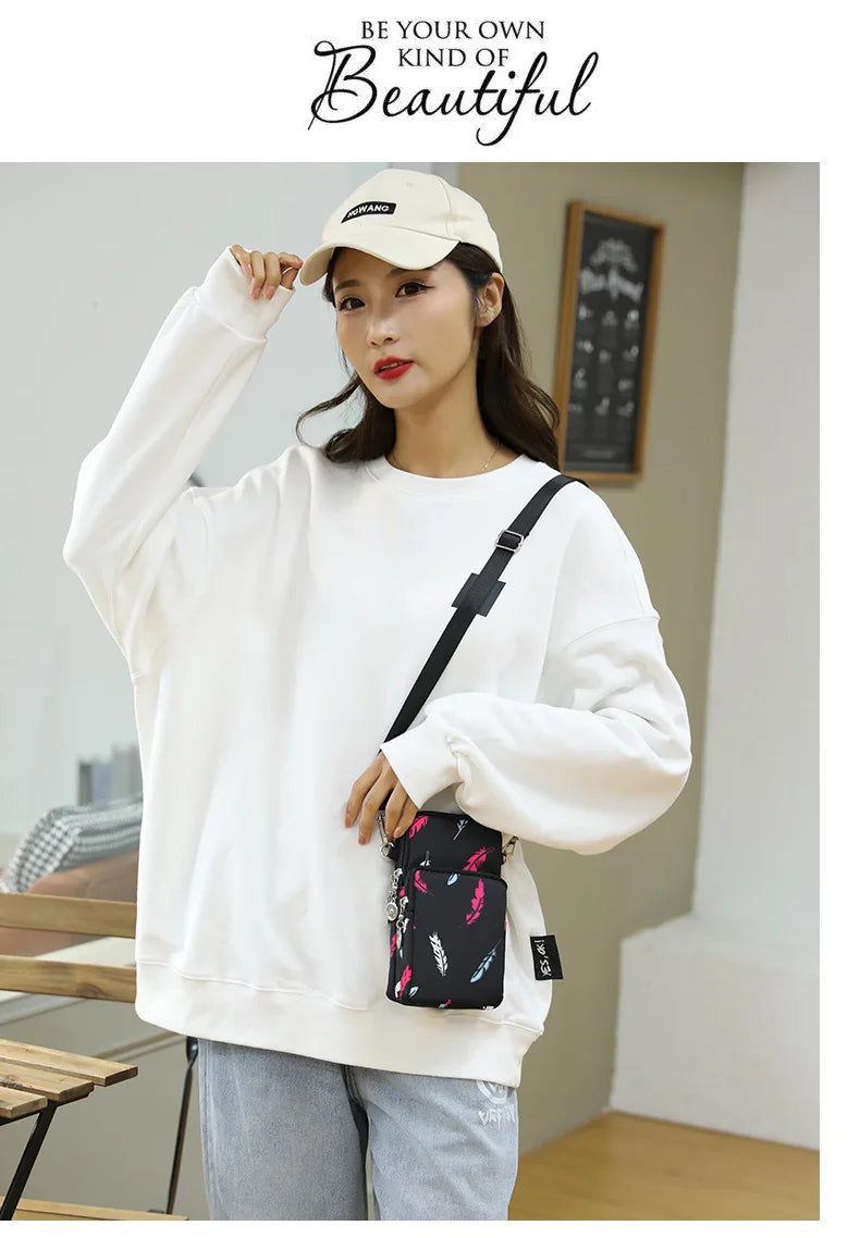 A woman wearing a white sweatshirt and light wash jeans holds a black nylon crossbody phone bag.