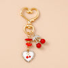 Gold-toned pearl bow heart keychain with red berries and white enamel detail