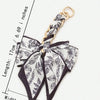 A black and white floral patterned fabric bow with a gold chain attached, used as an adjustable bag strap.