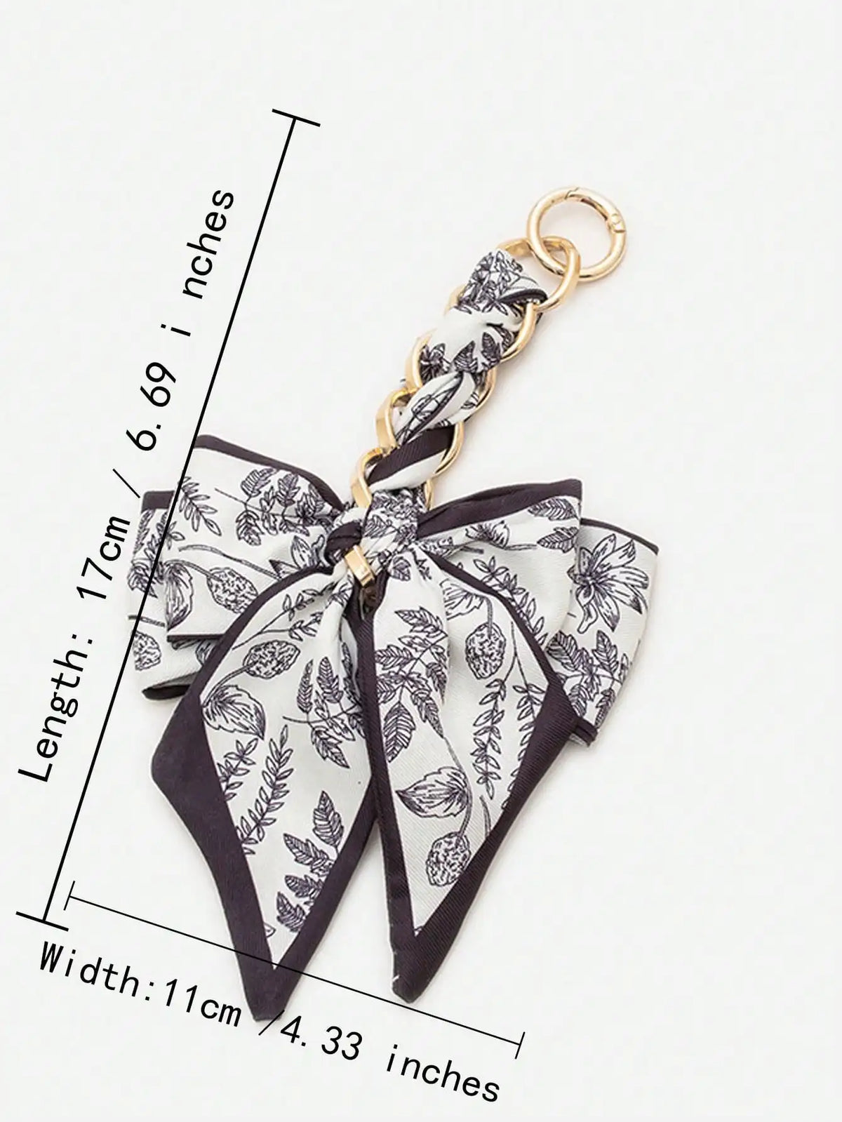 A black and white floral patterned fabric bow with a gold chain attached, used as an adjustable bag strap.