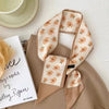 Foulard de cheveux floral en soie beige drapé sur un tissu marron, à côté d'un carnet.