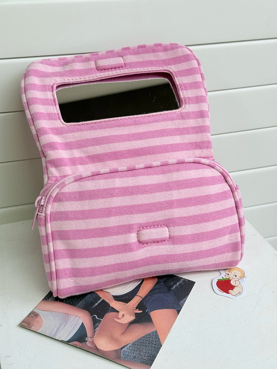 A pink striped Y2K makeup bag with a clear window and zipper is shown on a white surface.