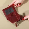 A close-up of a maroon PU leather card wallet with a double zip closure being held by a hand.