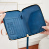 A hand holds an open blue RFID-blocking passport wallet with a zipper closure.