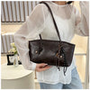 A woman holds a classic brown PU leather tote bag against a white sheer blouse and light blue jeans.