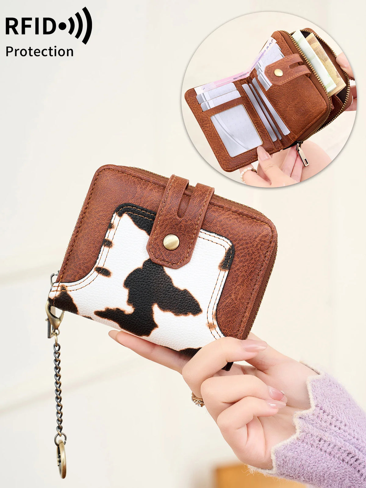 A brown leather bifold wallet with a white cow print design is shown being held, demonstrating RFID protection.