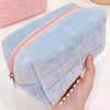 A light blue quilted cosmetic storage pouch with a pink zipper is held in a hand.