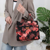 A woman holds a black floral patterned cloth tote bag with pink and red roses against a light background.
