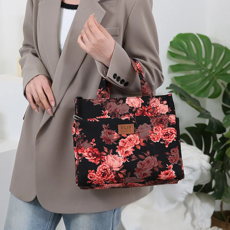 A woman holds a black floral patterned cloth tote bag with pink and red roses against a light background.