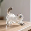 A clear glass figurine of a white cat with gray and blue eyes sitting on a wooden surface.