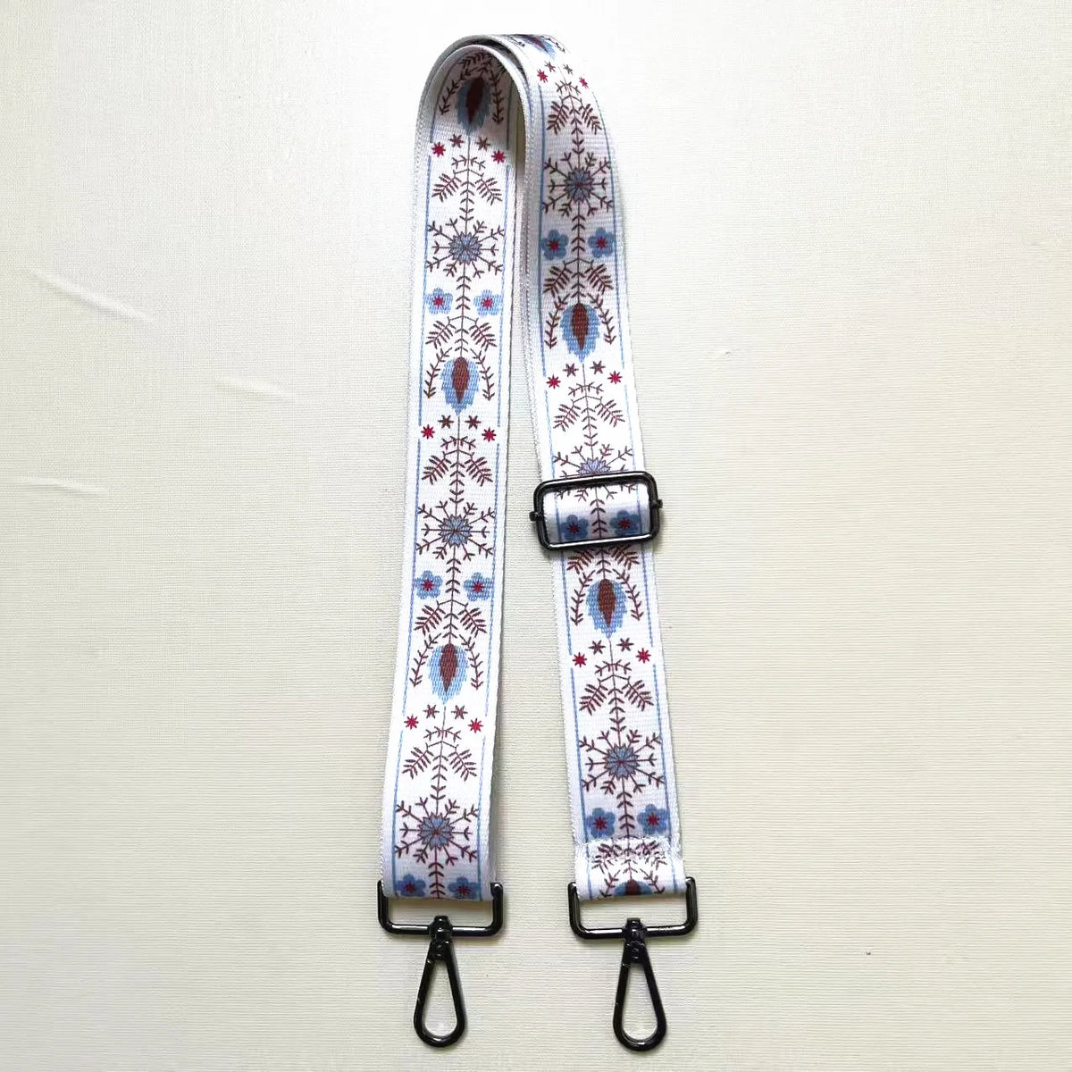 A white and blue patterned textile replacement bag strap with a silver buckle and metal clasps.