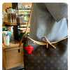 Un sac brun foncé à motif avec un charme de fraise, exposé sur une manche gris clair.