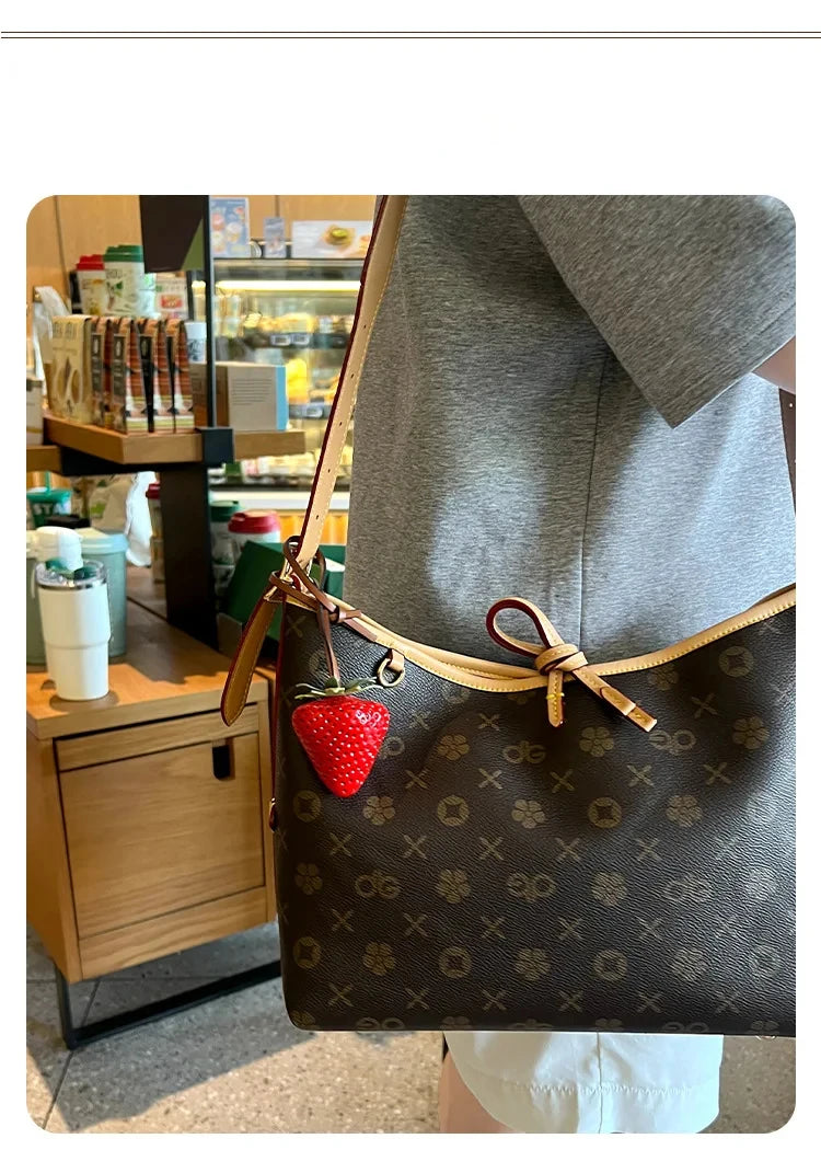 Un sac brun foncé à motif avec un charme de fraise, exposé sur une manche gris clair.
