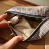 Une main ouvre une pochette de rangement cosmétique à rayures pour révéler la doublure intérieure.