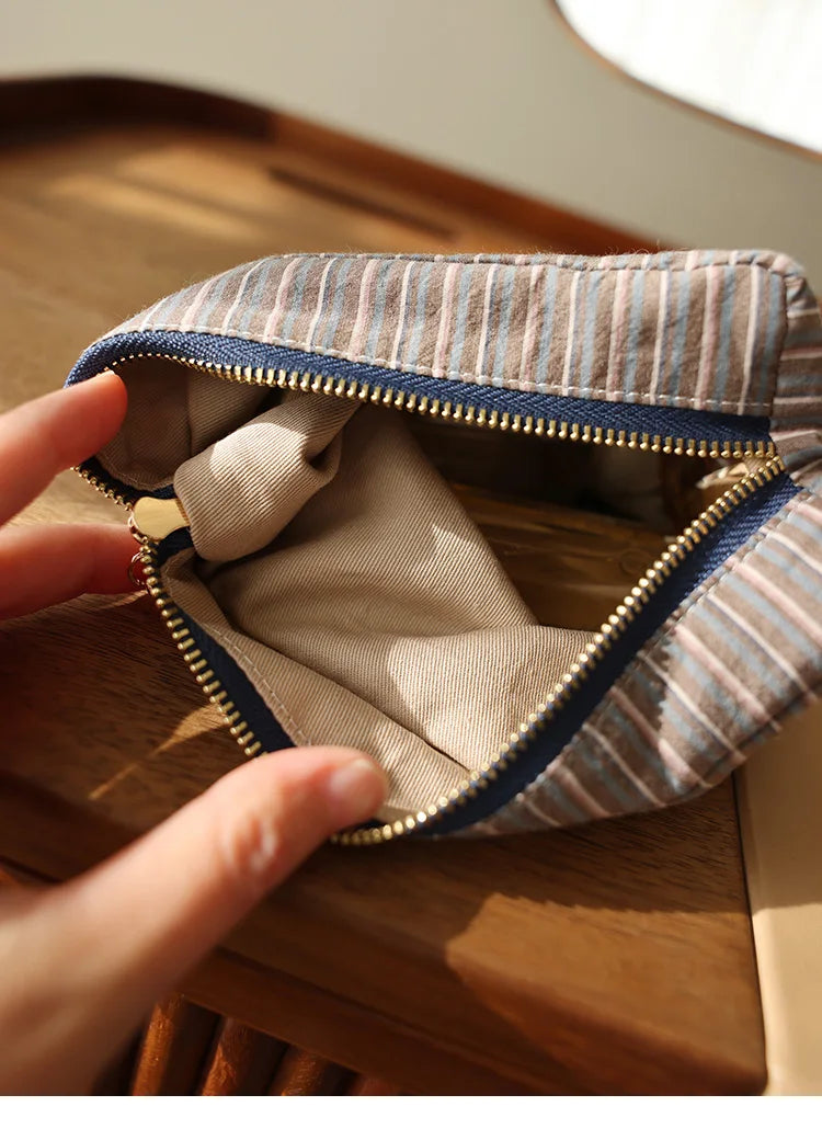 Une main ouvre une pochette de rangement cosmétique à rayures pour révéler la doublure intérieure.