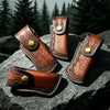 Three brown leather knife sheaths with decorative stitching and brass buttons resting on a dark rock.