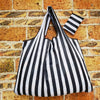 A black and white striped reusable shopping bag hanging against a brick wall.