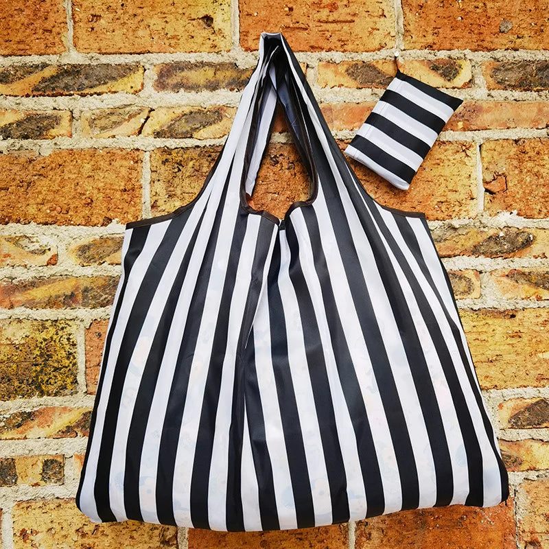 A black and white striped reusable shopping bag hanging against a brick wall.