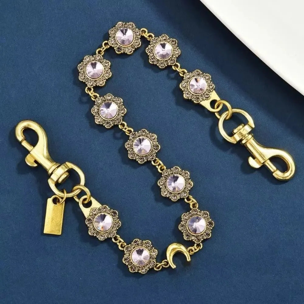 Gold-toned crystal petal keychain with rhinestone charm displayed on a dark blue velvet background.