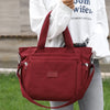 A maroon durable nylon tote bag with a shoulder strap is held by a person in a white shirt.