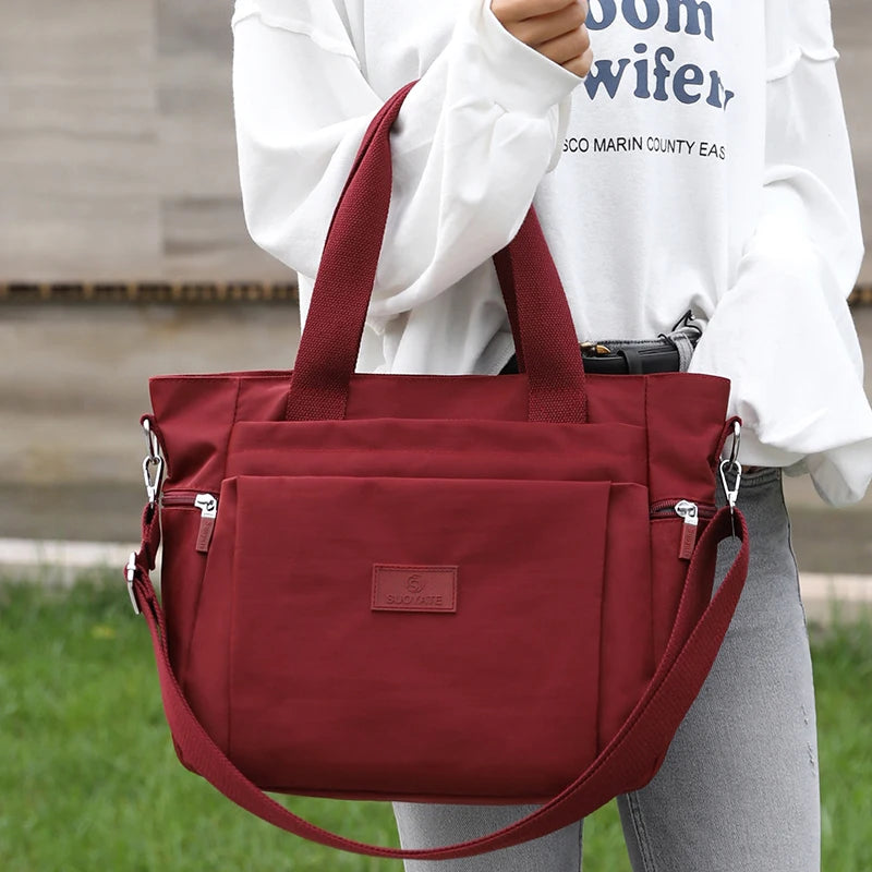 A maroon durable nylon tote bag with a shoulder strap is held by a person in a white shirt.