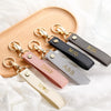 A collection of personalized leather wristlet keychains with various initials and designs displayed on a wooden board.