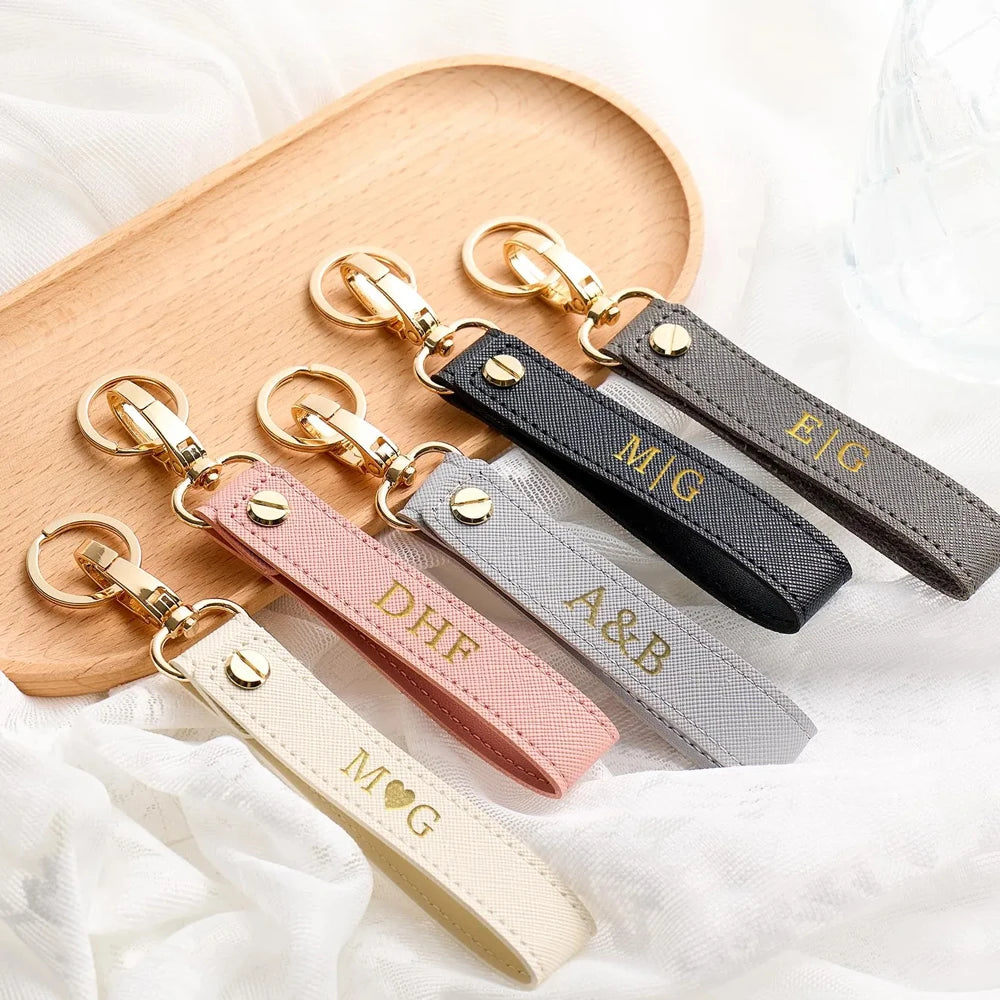A collection of personalized leather wristlet keychains with various initials and designs displayed on a wooden board.