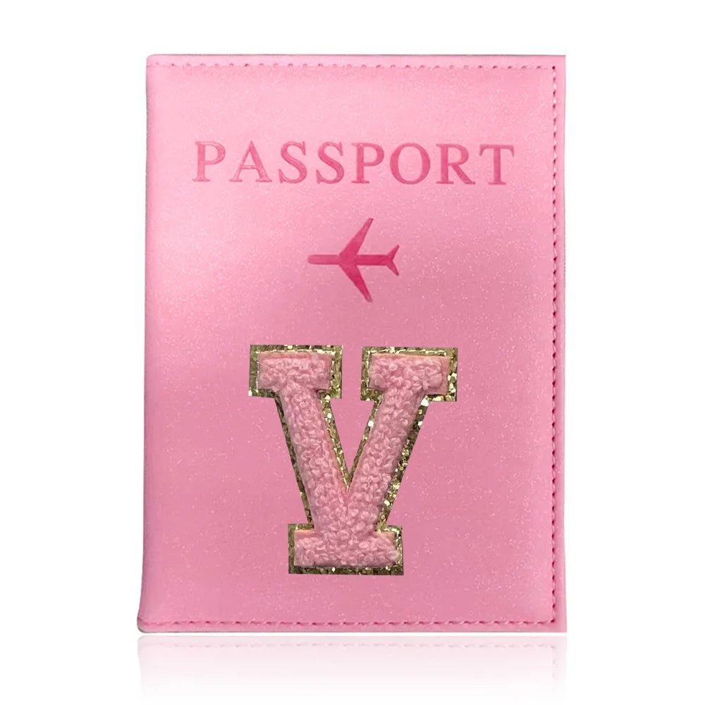 A pink leather passport holder with a gold initial V and a pink airplane symbol.