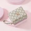 A light green letter zipper wristlet wallet with a gold monogram is displayed on a pink surface.