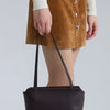 A woman is holding a dark brown leather mini shoulder bag with adjustable straps.
