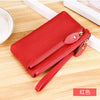A red genuine leather wristlet clutch wallet with a zipper closure lying on a wooden surface.