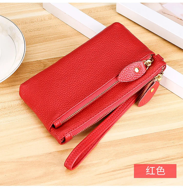 A red genuine leather wristlet clutch wallet with a zipper closure lying on a wooden surface.