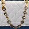 A gold-toned necklace featuring crystal petal charms and rhinestones displayed against a white quilted leather bag.