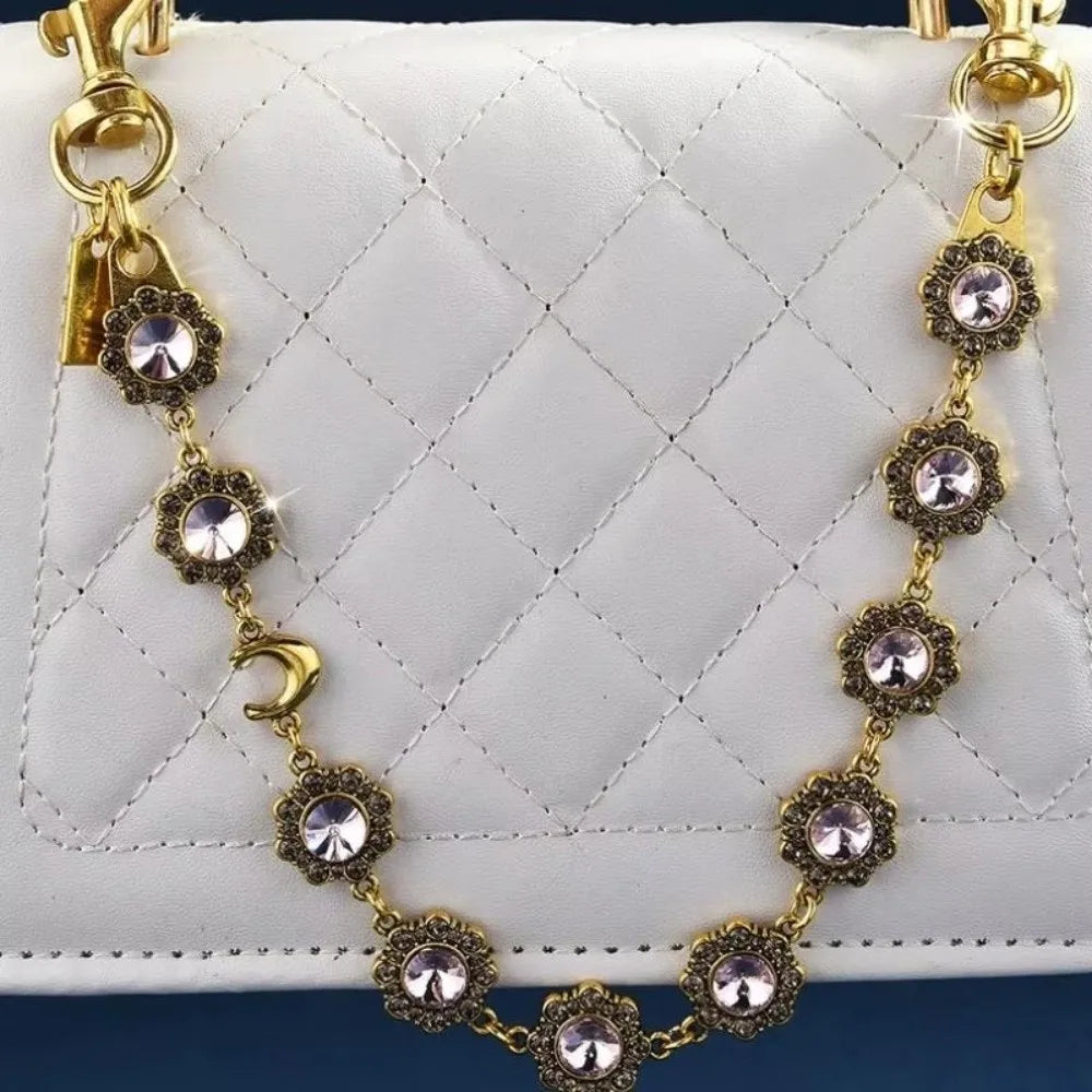 A gold-toned necklace featuring crystal petal charms and rhinestones displayed against a white quilted leather bag.