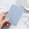 A hand holds a light blue ultra-thin multi-slot card wallet on a white marble surface.
