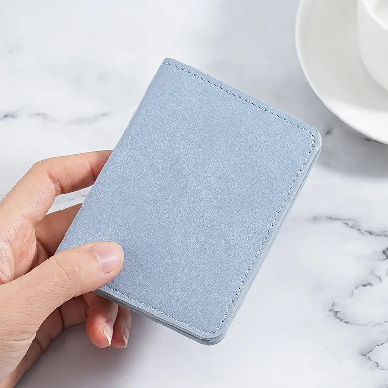 A hand holds a light blue ultra-thin multi-slot card wallet on a white marble surface.