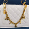 Gold chain necklace with a cherry flower pendant resting on a white quilted bag.