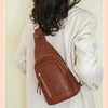 A woman is holding a brown PU leather crossbody sling bag against a light background.