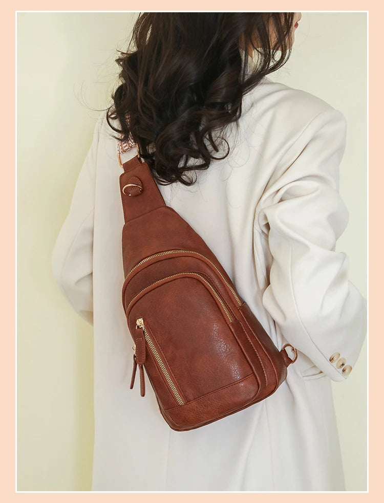 A woman is holding a brown PU leather crossbody sling bag against a light background.