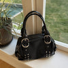 A black PU leather shoulder bag with silver rivets and hardware resting on a windowsill next to a potted plant.